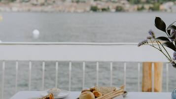 A dining table with various dishes and a cup of coffee, overlooking a body of water and mountains.