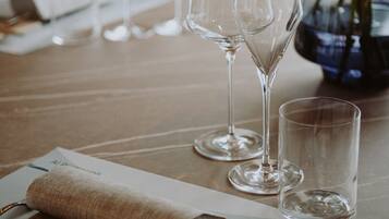 Una mesa dispuesta con servilleta, cubiertos y copas de vino, con un florero en el fondo.