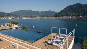 A swimming pool with lounge chairs on a deck overlooking a lake with boats and a cityscape in the background. - Ah Porticcioli boutique apartments (San Felice del Benaco)