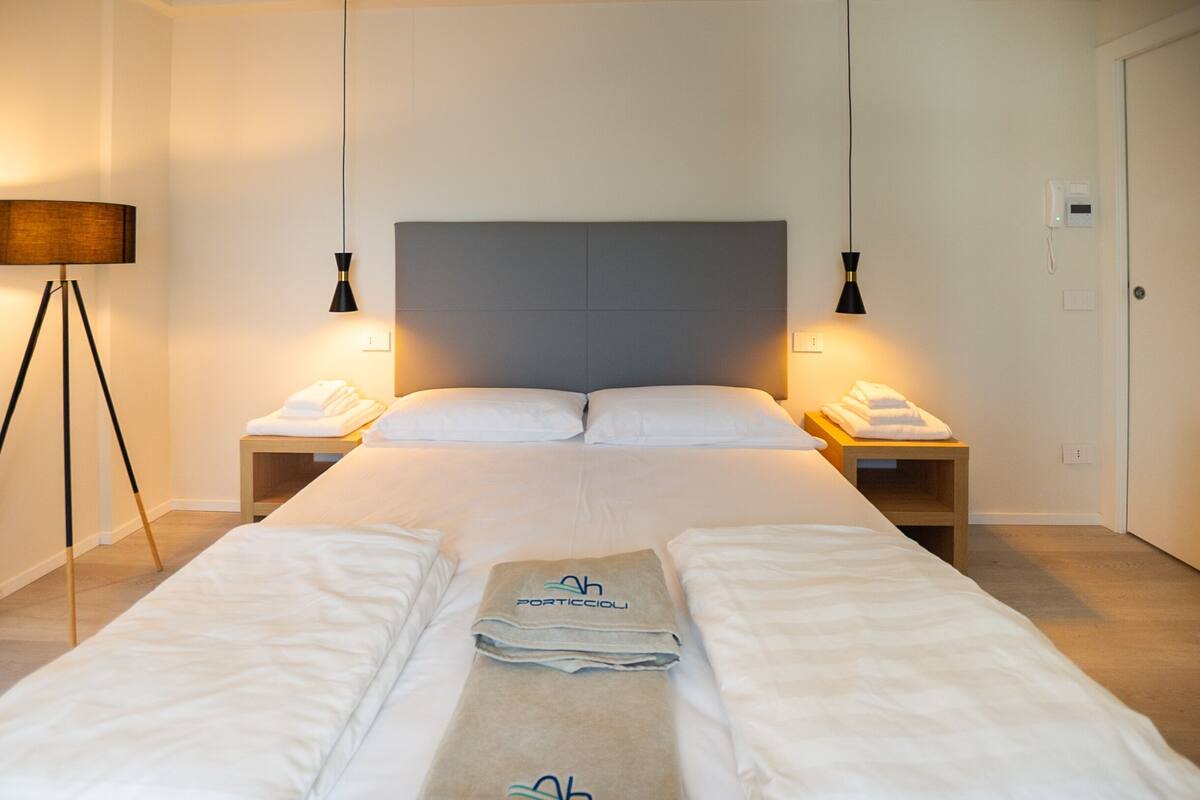 A hotel room with a large bed, two bedside tables, a lamp, and a folded towel on the bed.