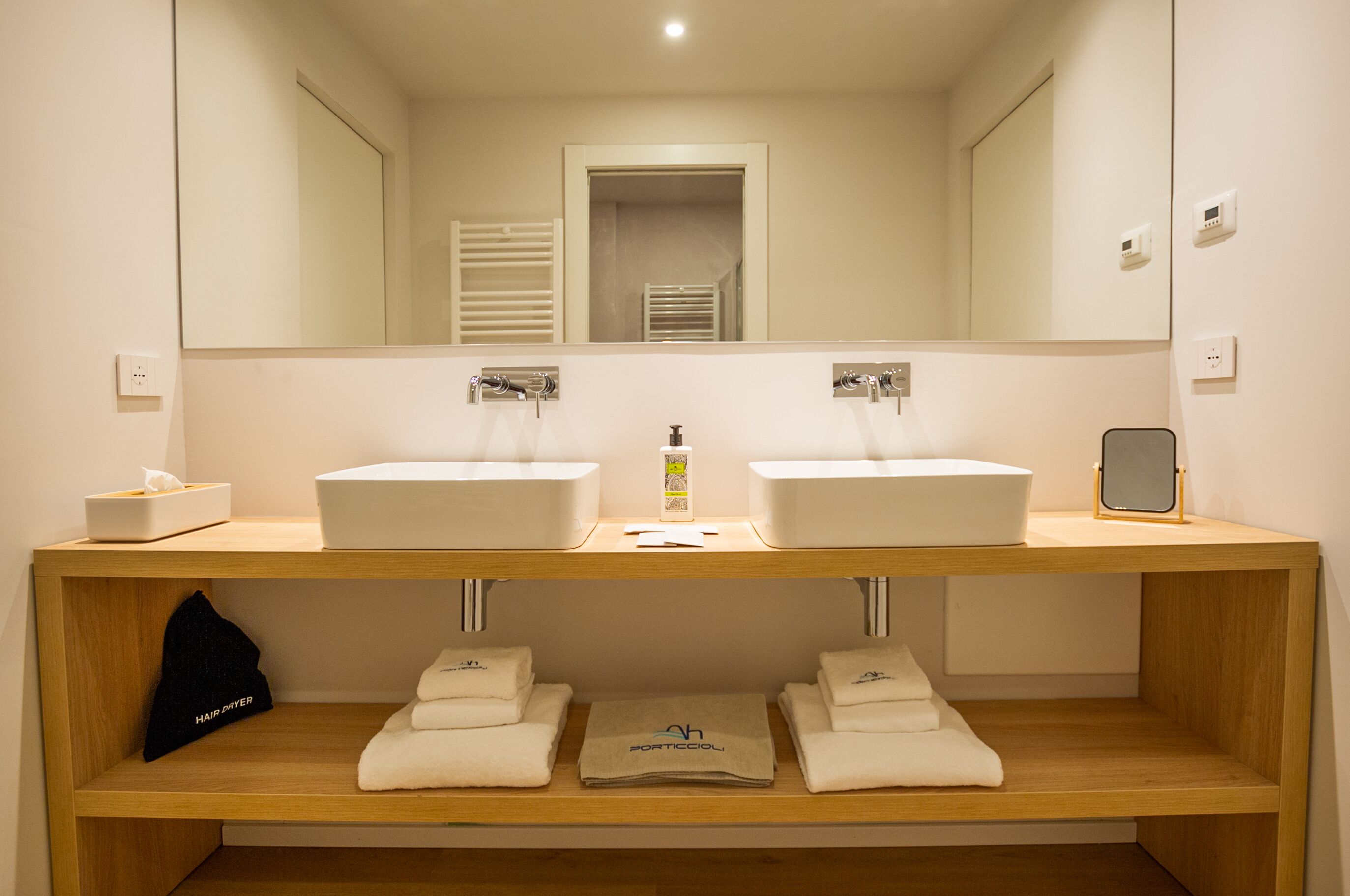 A bathroom with two sinks, a mirror, and a shelf with towels.