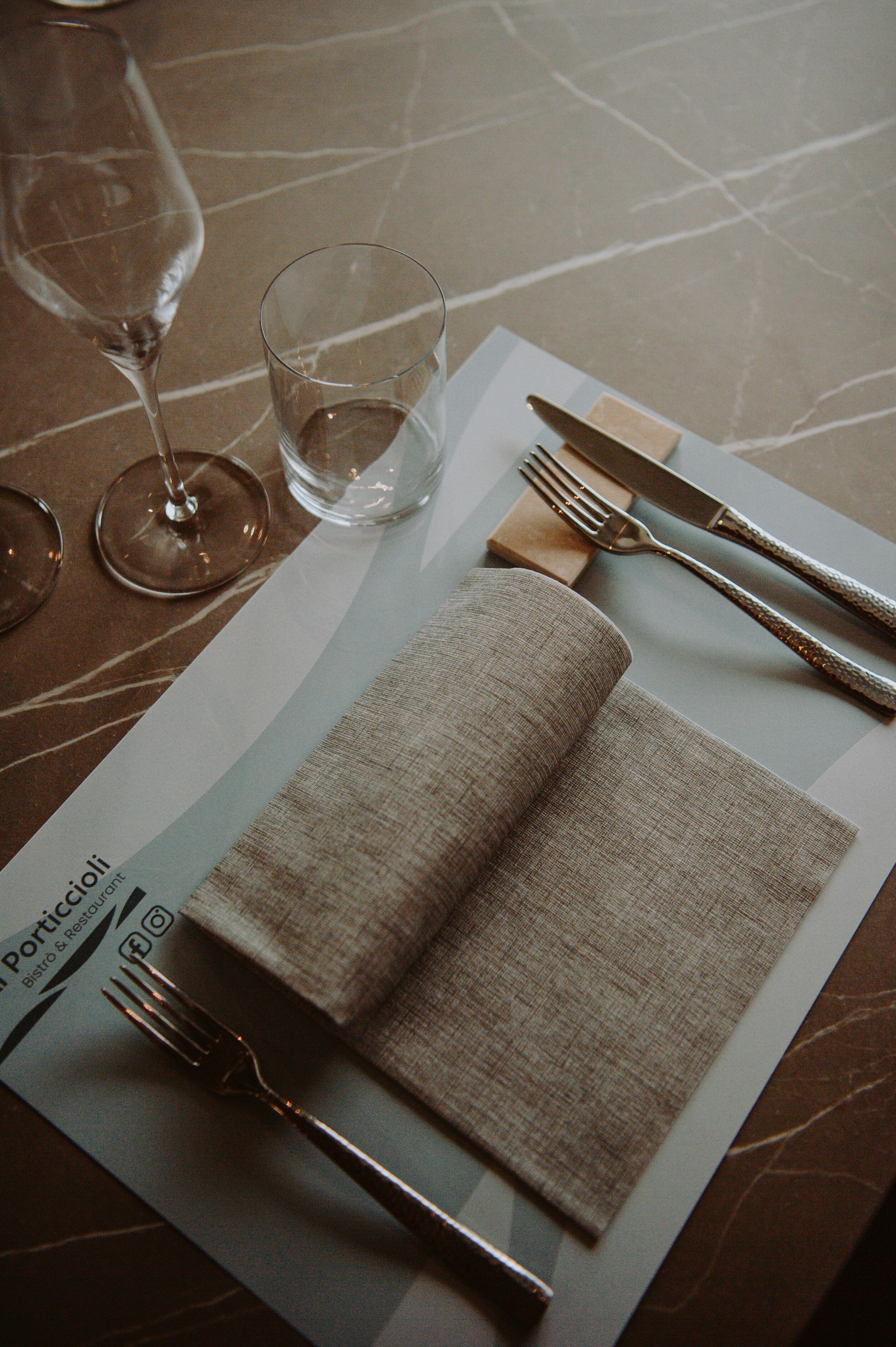 A table set with a folded napkin, a fork, a knife, and a glass of water on a marble table.