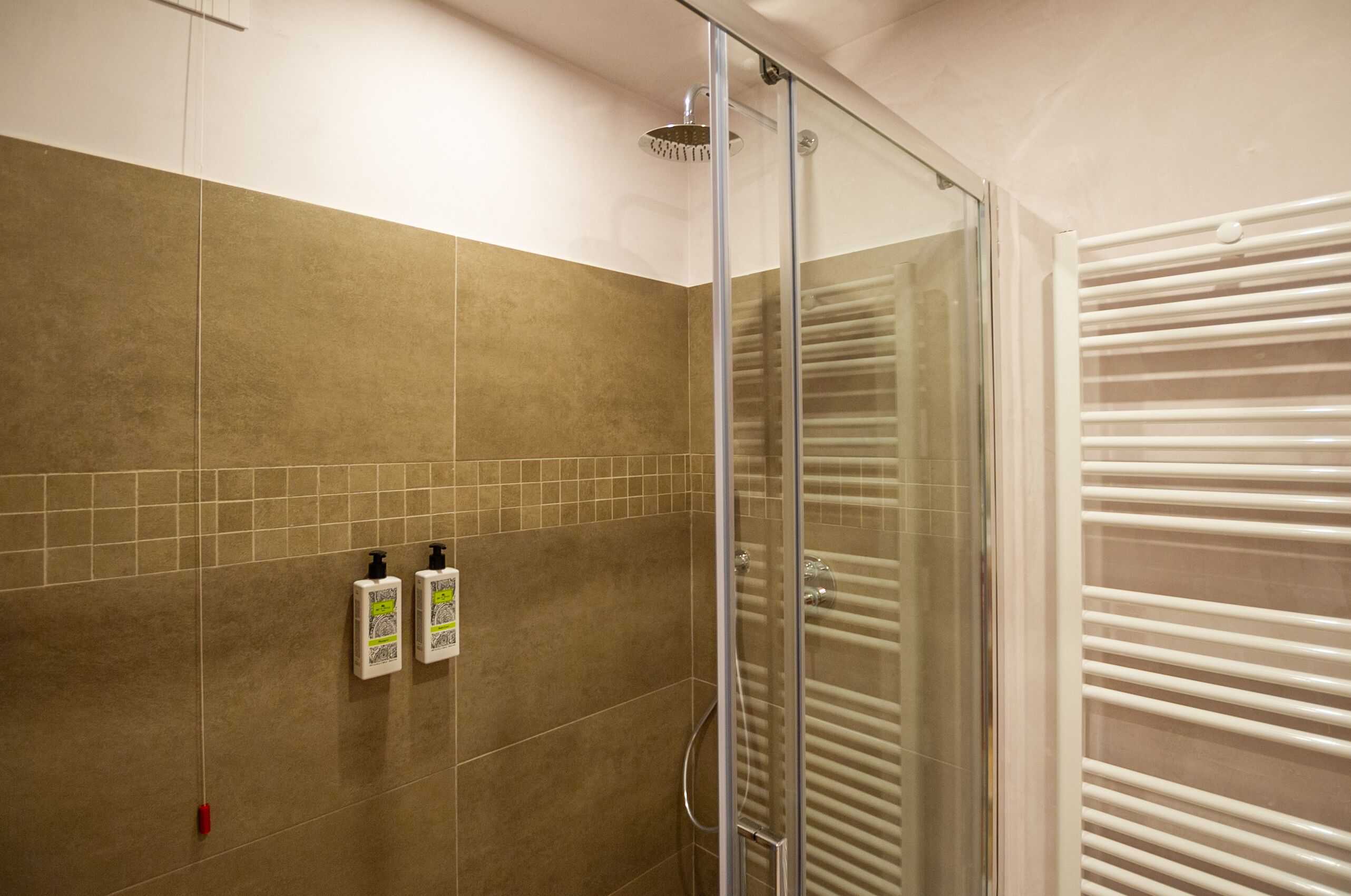 Un área de ducha con puerta de vidrio, paredes de azulejos color beige y un toallero blanco.