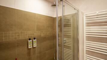 Un área de ducha con puerta de vidrio, paredes de azulejos color beige y un toallero blanco.