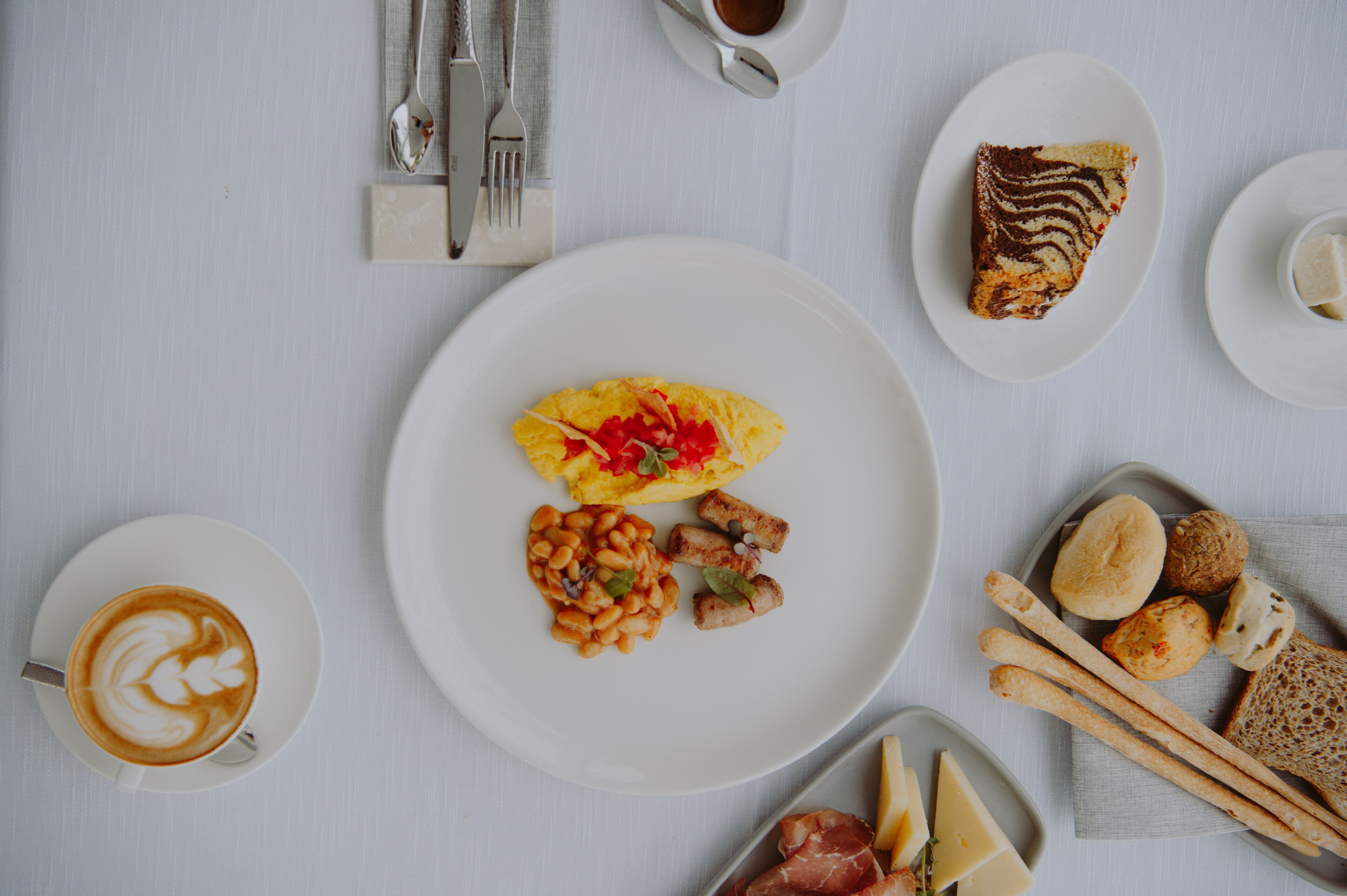 A breakfast setting with a plate of scrambled eggs, beans, and meat, a slice of cake, and a cup of coffee.