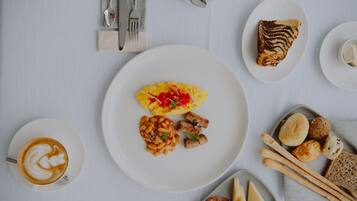 A breakfast setting with a plate of scrambled eggs, beans, and meat, a slice of cake, and a cup of coffee.