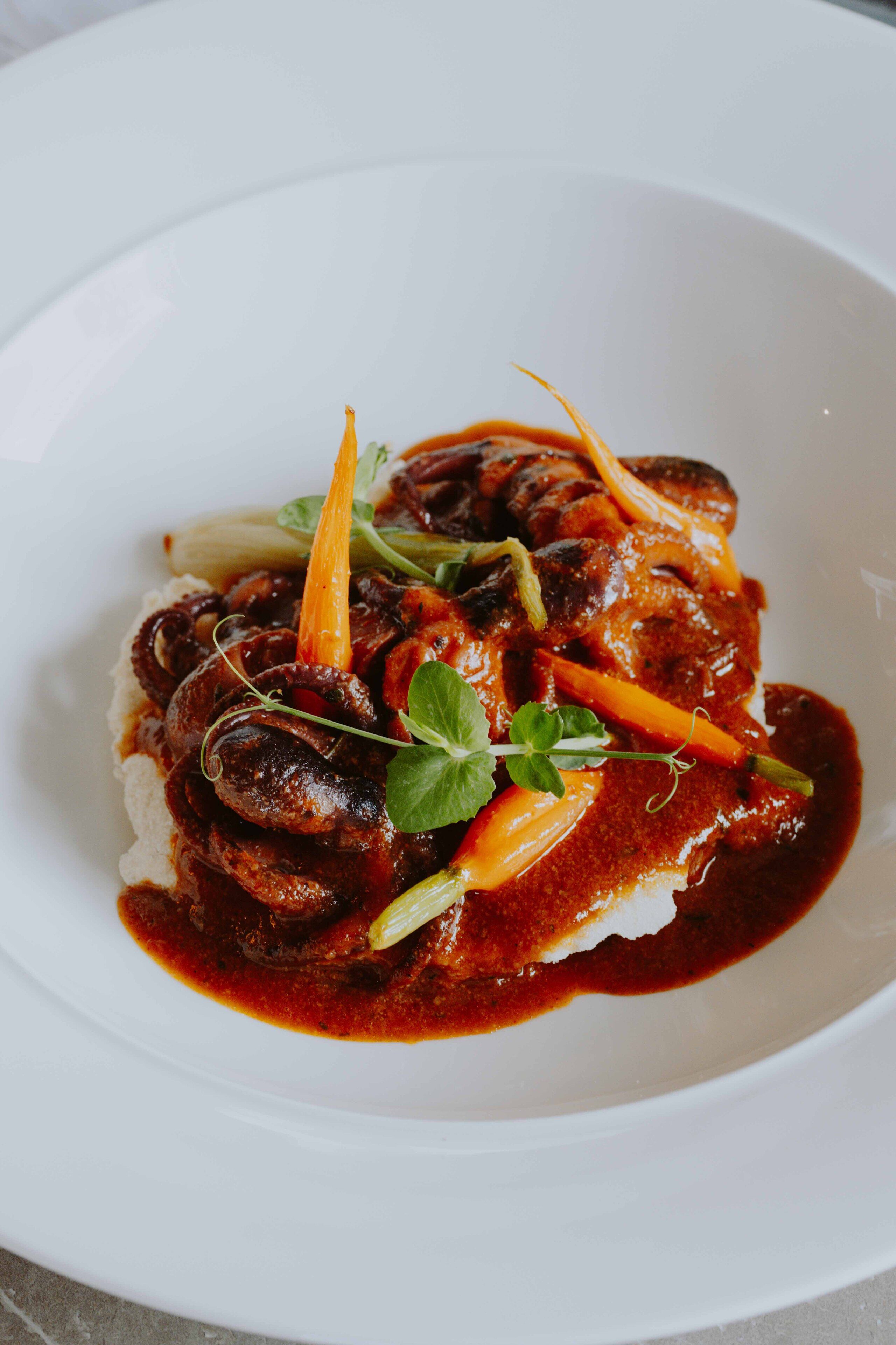 A white plate with a dish of meat, vegetables, and sauce.