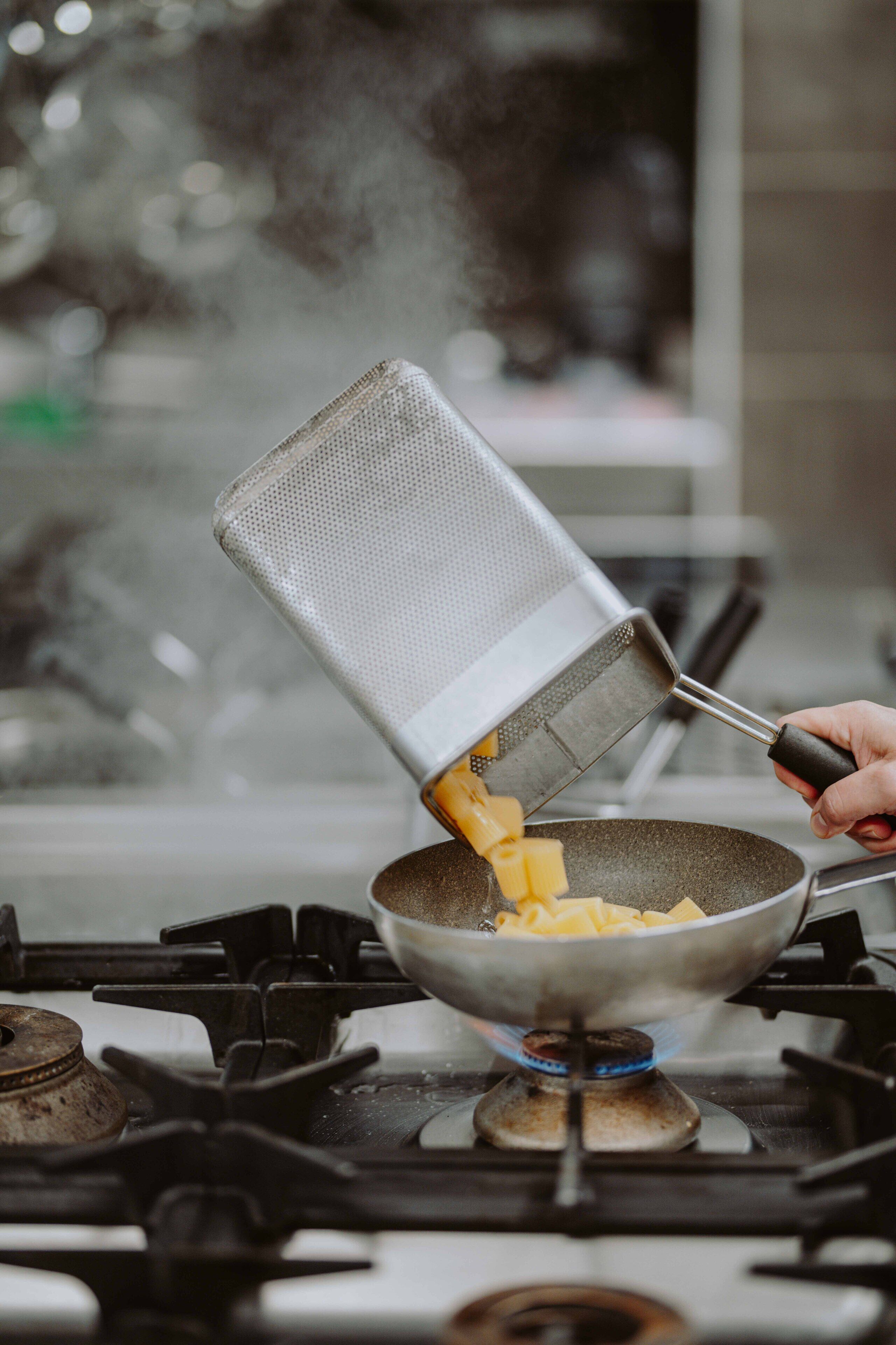 A hand pouring grated cheese into a hot pan on a stove.