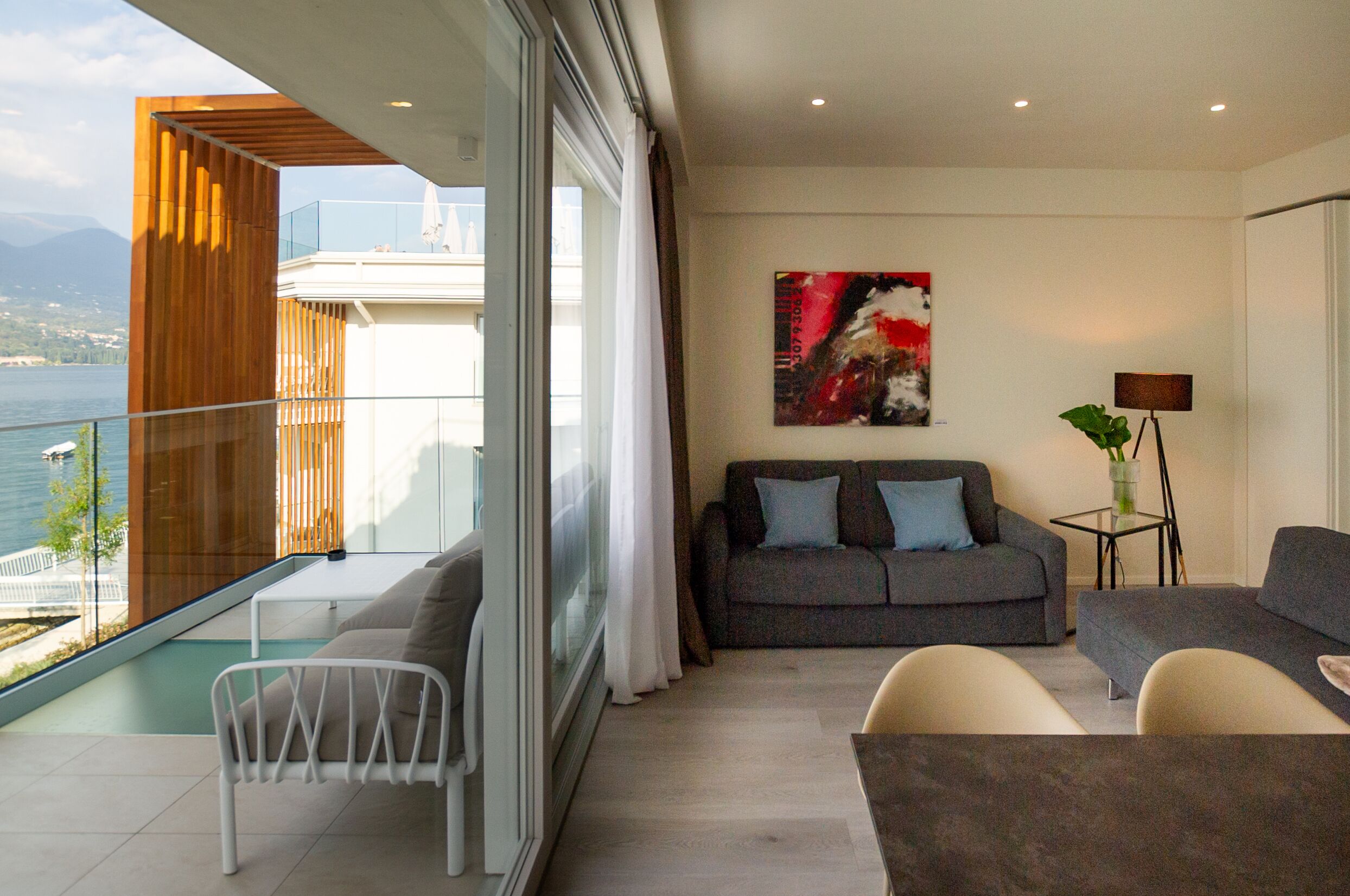 A modern living room with a balcony overlooking a body of water and mountains.