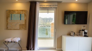 A hotel room with a bed, a small table with a kettle and a coffee machine, a TV on the wall, and a view of a body of water through a large window. - Ah Porticcioli boutique apartments (San Felice del Benaco)