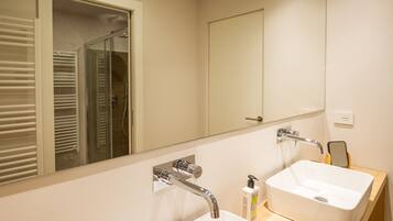 A modern bathroom with a large mirror, a white sink, and a shower area.