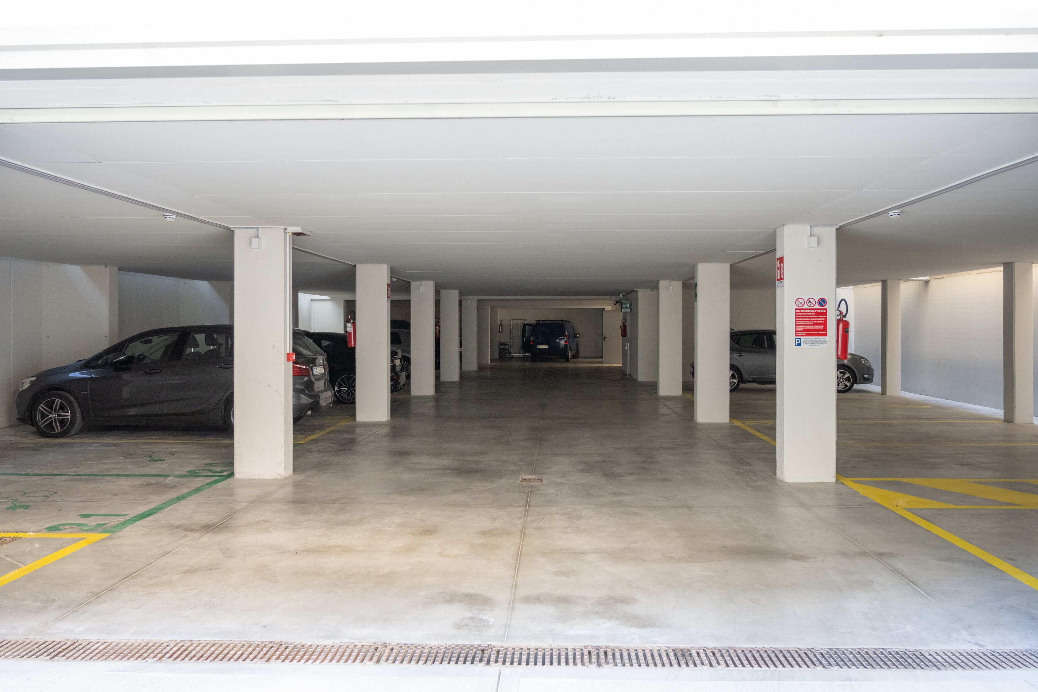 A multi-level parking garage with several cars parked, concrete pillars, and clear floor markings.