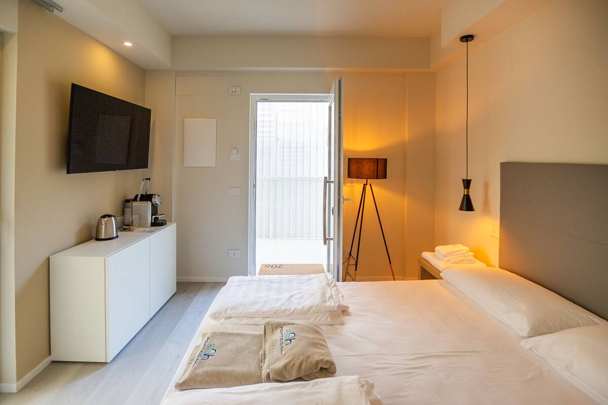 A hotel room with a bed, bedside table, lamp, and a TV mounted on the wall.