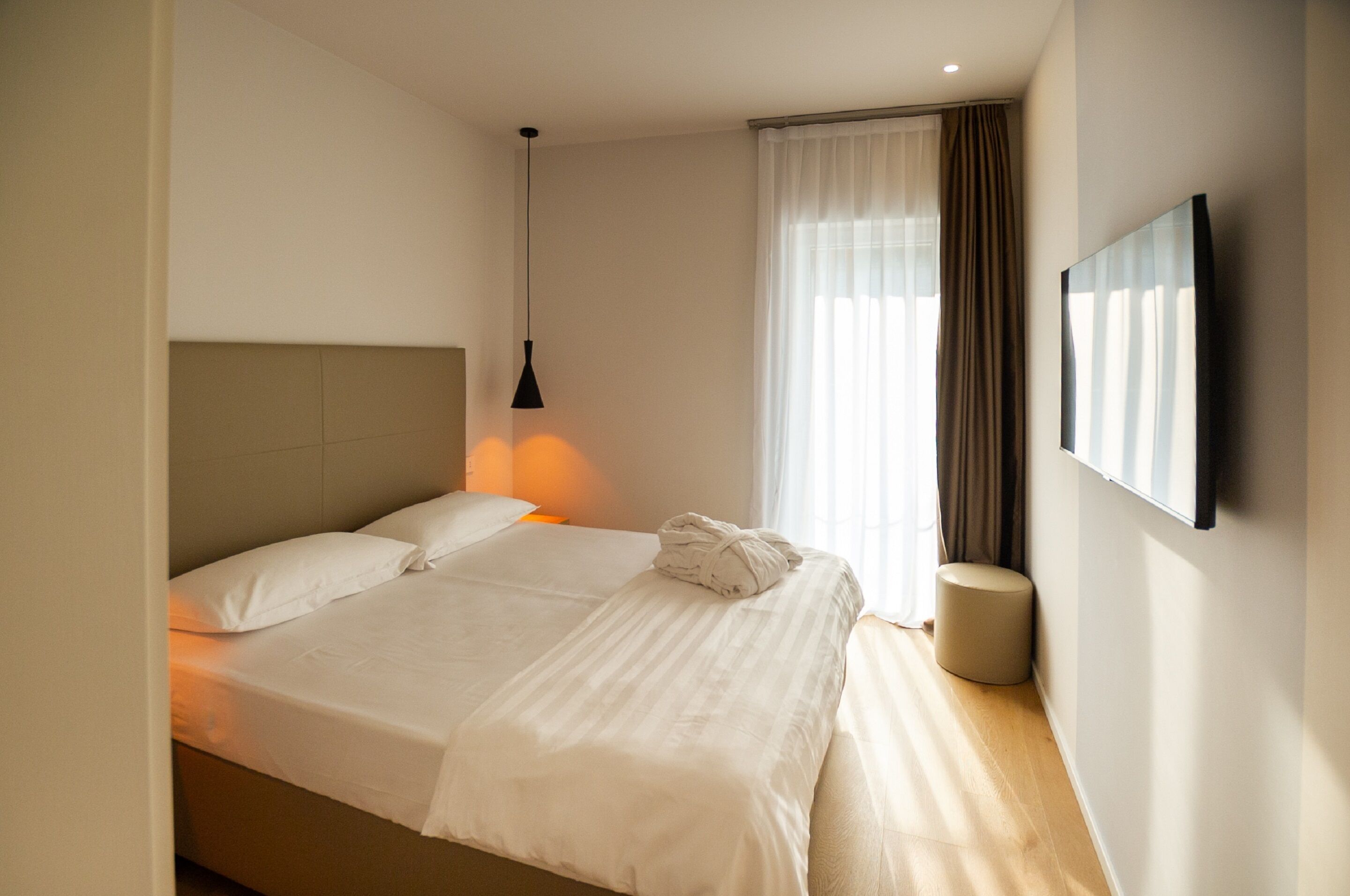 A hotel room with a large bed, a bedside lamp, a round bedside table, and a flat-screen TV mounted on the wall.