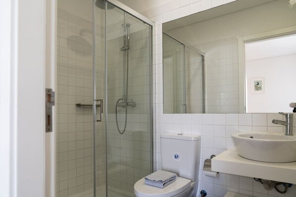 Un baño moderno con ducha de vidrio, inodoro blanco y lavamanos con espejo.