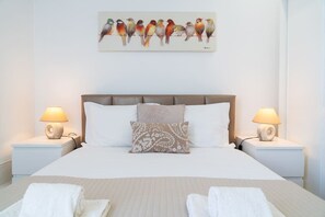 Un lit bien fait, agrémenté d’un coussin à motifs, de deux lampes de chevet et d’un tableau représentant un oiseau, accroché au mur.