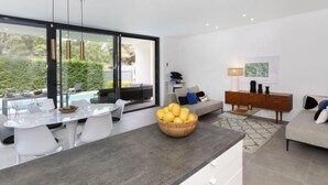 A modern kitchen with a large island, a dining area with white chairs, a grey sofa, and a wooden sideboard. - Vacation home Alyssa by Interhome (St Feliu de Guíxols)