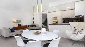 A modern living room with a round white table, white chairs, and a sofa. There is a kitchen area with white cabinets and a dining area with a white table and chairs. - Vacation home Alyssa by Interhome (St Feliu de Guíxols)