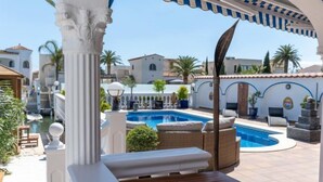 Area piscina con solarium in legno, lettini e zona relax coperta con tenda a righe.