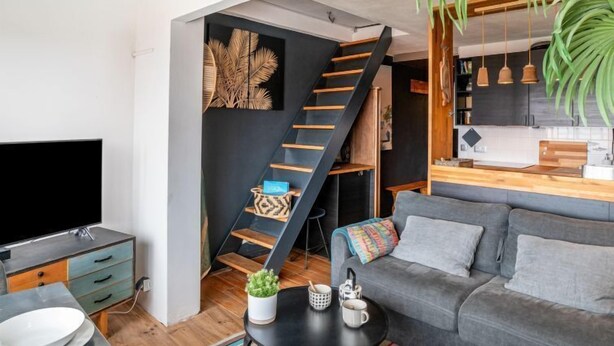 Ein modernes Wohnzimmer mit Sofa, Couchtisch, Fernseher, einer Treppe und einer Küchenzeile.