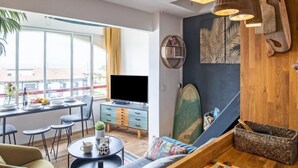 Ein modernes Wohnzimmer mit Essbereich, großen Fenstern und einem Fernseher.