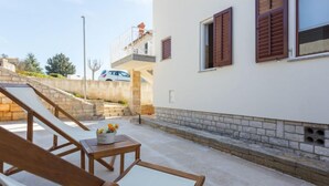 Un edificio moderno con una escalera de piedra que lleva a un balcón, una pared blanca con contraventanas de madera y una pequeña mesa con una maceta.