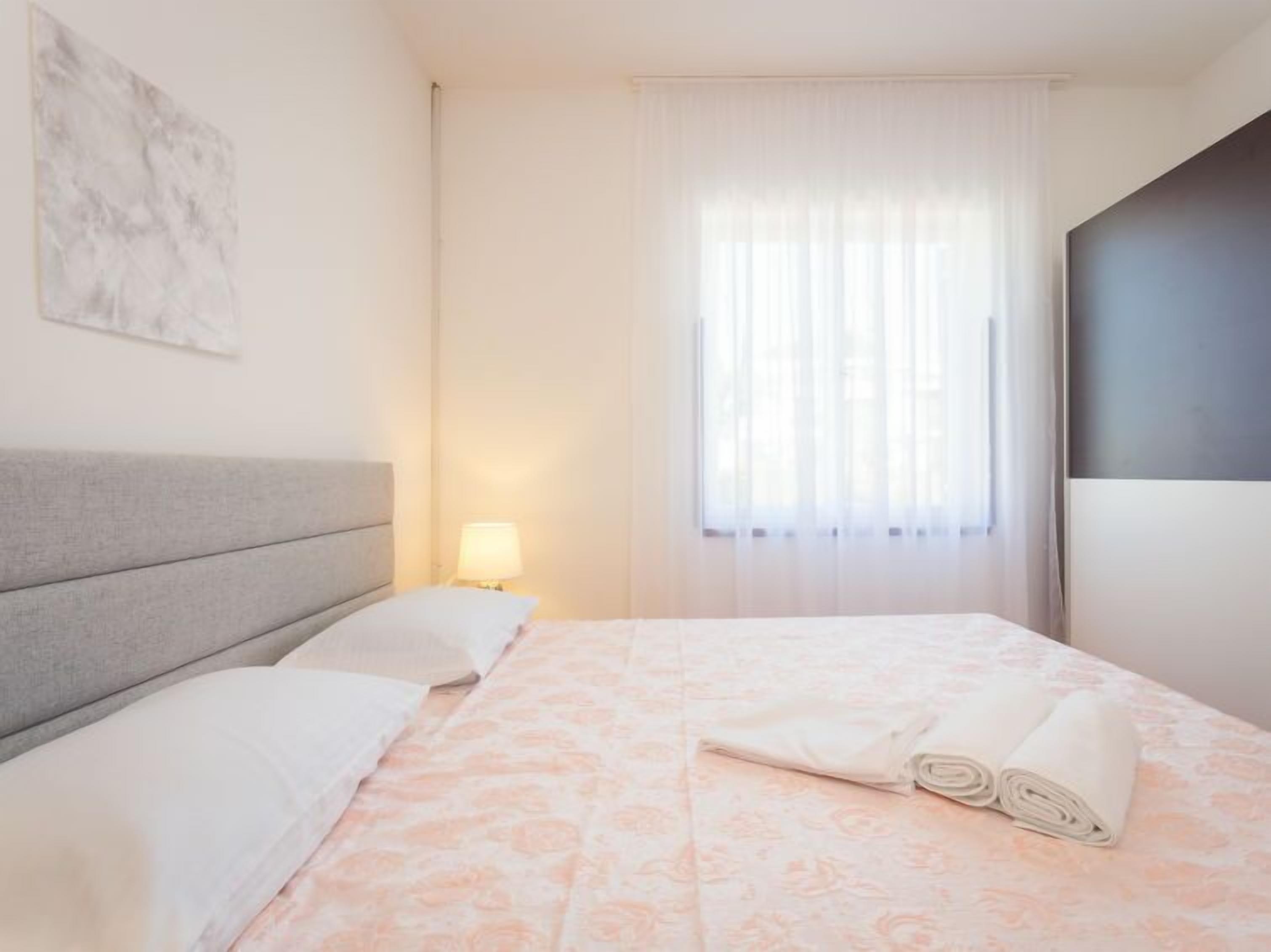 Een hotelkamer met een bed, nachtkastje, lamp, raam met gordijnen en een schilderij aan de muur.