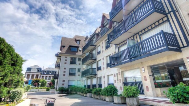 Un edificio residencial de varios pisos con balcones, zona de estacionamiento y zonas verdes circundantes.