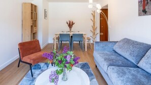 Una sala de estar con un sofá azul, una silla roja, una mesa de comedor con sillas, un aparador de madera y un jarrón con flores.