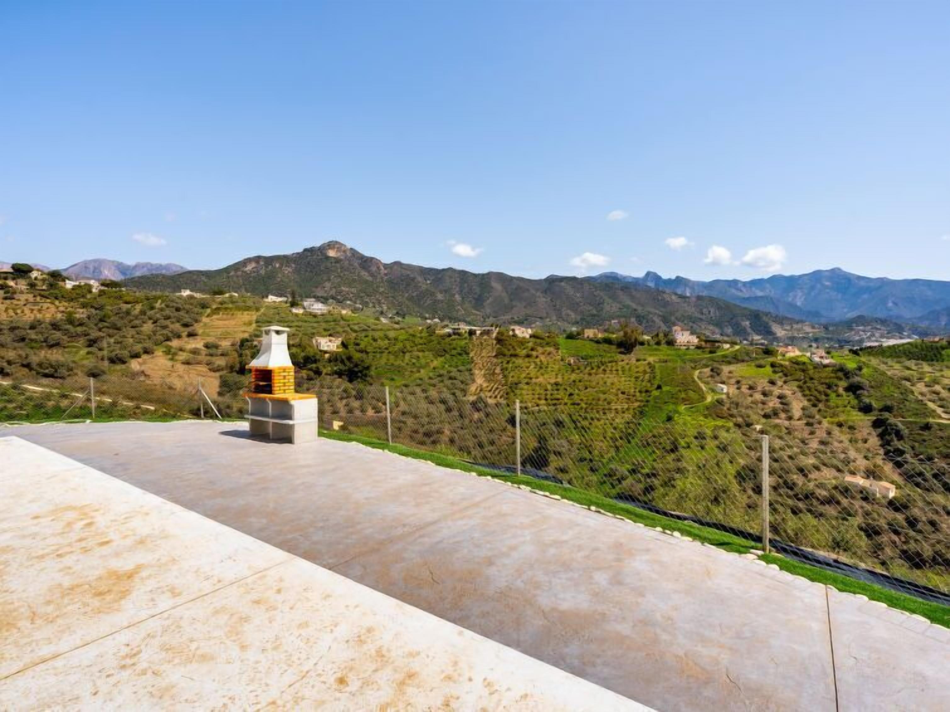 A terrace with a chimney, overlooking a hilly landscape with houses and vineyards.