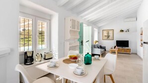 A bright, white room with a dining table set for two, a television, and a sofa. - Las Vistas by Interhome (Torrox Costa)