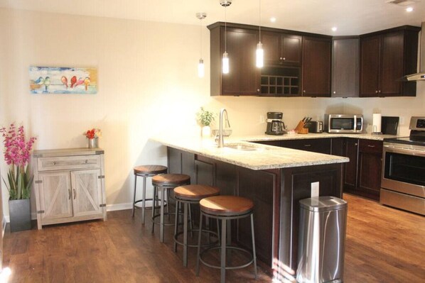 A modern kitchen with dark wood cabinets, a central island with stools, stainless steel appliances, and a decorative painting on the wall.