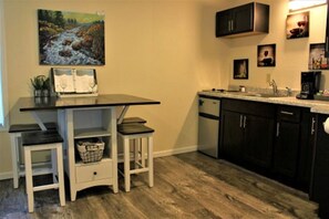 A compact kitchen with a dining area, featuring a table, two stools, a small sink, and dark cabinets.
