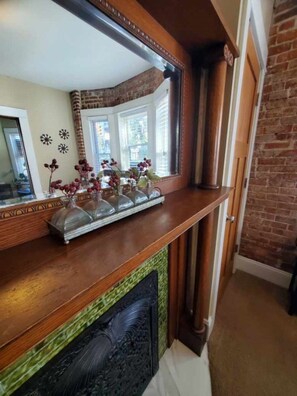 A wooden mantel with a mirror above it, reflecting a window and a brick wall. - 131 Cedar 2 · Chic 2BR Urban Retreat | Downtown Kalamazoo (Kalamazoo)