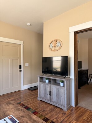 A living room with a flat-screen TV on a wooden stand, a door, and a wall-mounted artwork.
