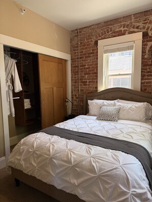 Un dormitorio con cama, armario, ventana y pared de ladrillo.