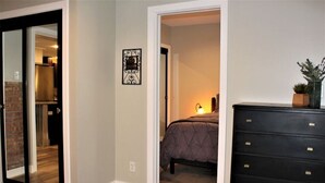 A bedroom with a bed, a dresser, and a door leading to another room. - 125 Cedar 1 · Apartment in Kalamazoo + WI-Fi + Garage + Laundry (Kalamazoo)