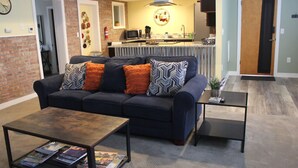 A living room with a dark blue sofa, two coffee tables, and a kitchen area in the background. - 125 Cedar 1 · Apartment in Kalamazoo + WI-Fi + Garage + Laundry (Kalamazoo)