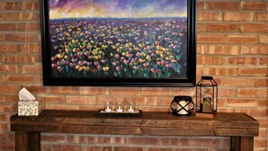 A framed painting of a field of flowers on a brick wall, a tissue box, and a candle holder on a wooden shelf. - 125 Cedar 1 · Apartment in Kalamazoo + WI-Fi + Garage + Laundry (Kalamazoo)