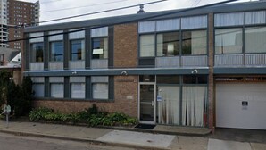 A two-story building with a brick facade, large windows, and a garage door. - 125 Cedar 1 · Apartment in Kalamazoo + WI-Fi + Garage + Laundry (Kalamazoo)