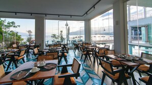 Ένας ευρύχωρος, εσωτερικός χώρος για φαγητό, με πολλά τραπέζια και καρέκλες, καθώς και μεγάλα παράθυρα που προσφέρουν θέα σε ένα ορεινό τοπίο.