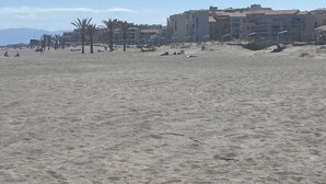 Ein sandiger Strand mit Palmen und im Hintergrund eine Reihe mehrstöckiger Gebäude.