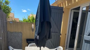 Ein Terrassenbereich im Freien mit Tisch und Stühlen, einem Sonnenschirm und einer Schiebetür.