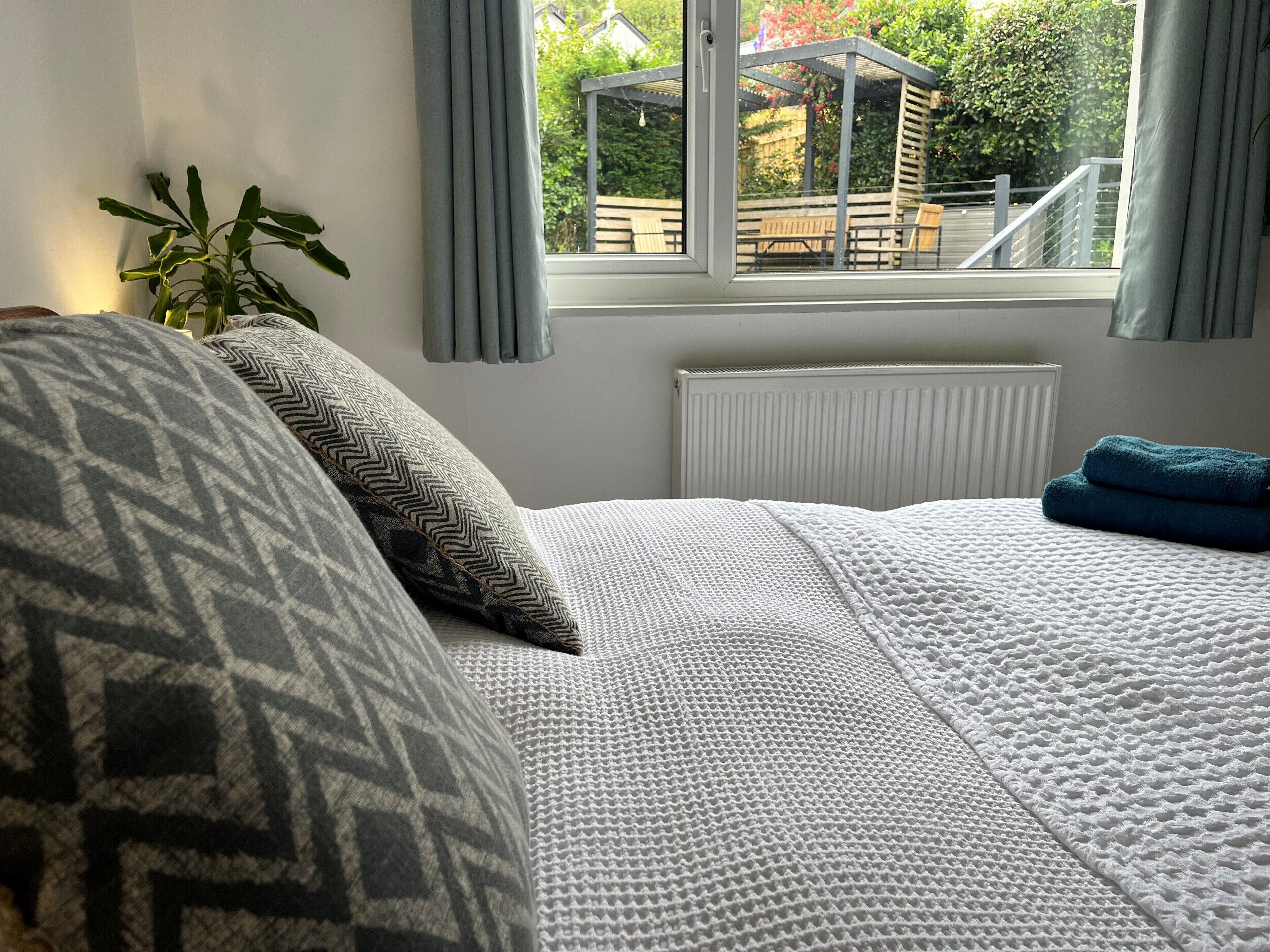 Une chambre à coucher avec un lit, une fenêtre avec des rideaux, un radiateur et une plante en pot.