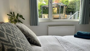 Ein Schlafzimmer mit Bett, einem Fenster mit Vorhängen, einem Heizkörper und einer Topfpflanze.