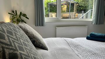 Une chambre à coucher avec un lit, une fenêtre avec des rideaux, un radiateur et une plante en pot.
