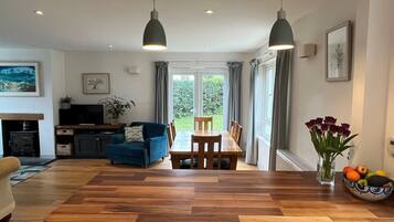 A modern kitchen with a wooden countertop, two pendant lights, a dining table with chairs, a blue sofa, a TV, and a fireplace.