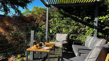 Une terrasse extérieure avec une table en bois, deux chaises grises rembourrées et une structure en forme de pergola.