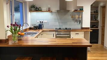 Une cuisine moderne dotée d’un îlot central, de plans de travail en bois et d’une cuisinière intégrée. L’îlot est agrémenté de trois tabourets, il y a un évier et une fenêtre offrant une belle vue.