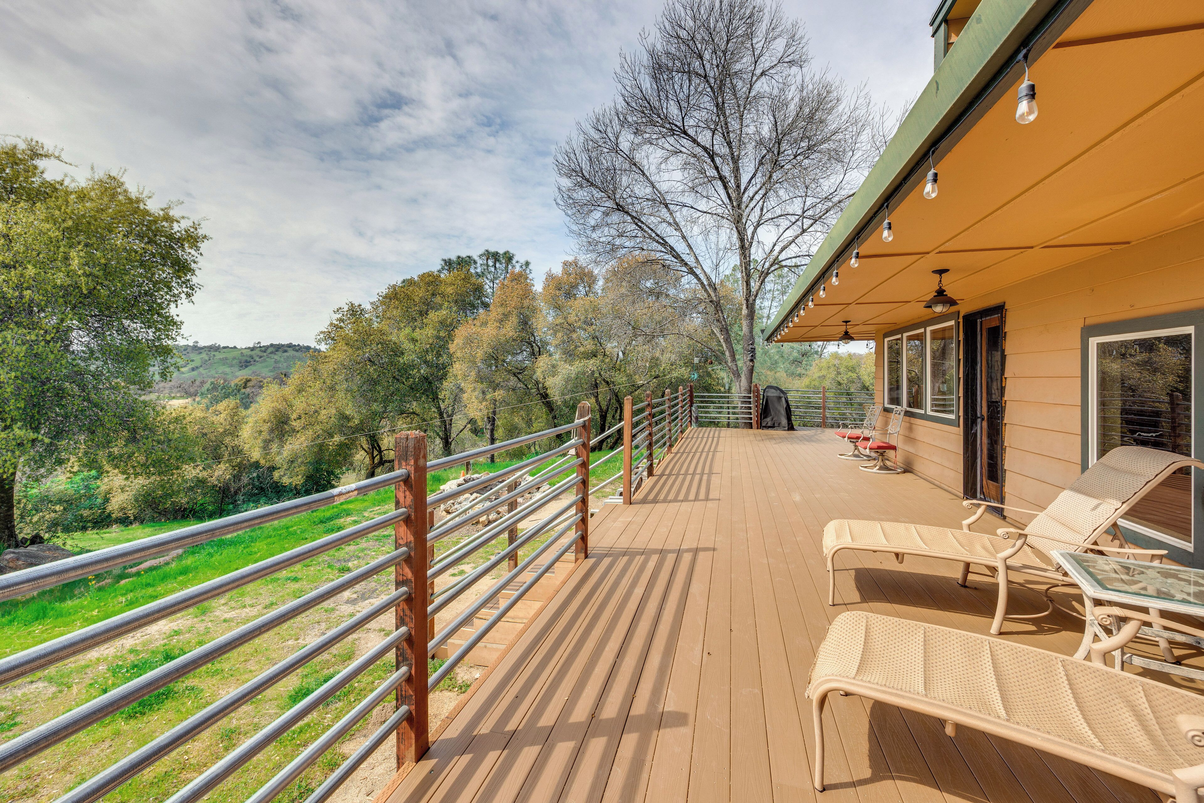 Eine Holzterrasse mit Liegestühlen und Geländer mit Blick auf eine grüne Landschaft.